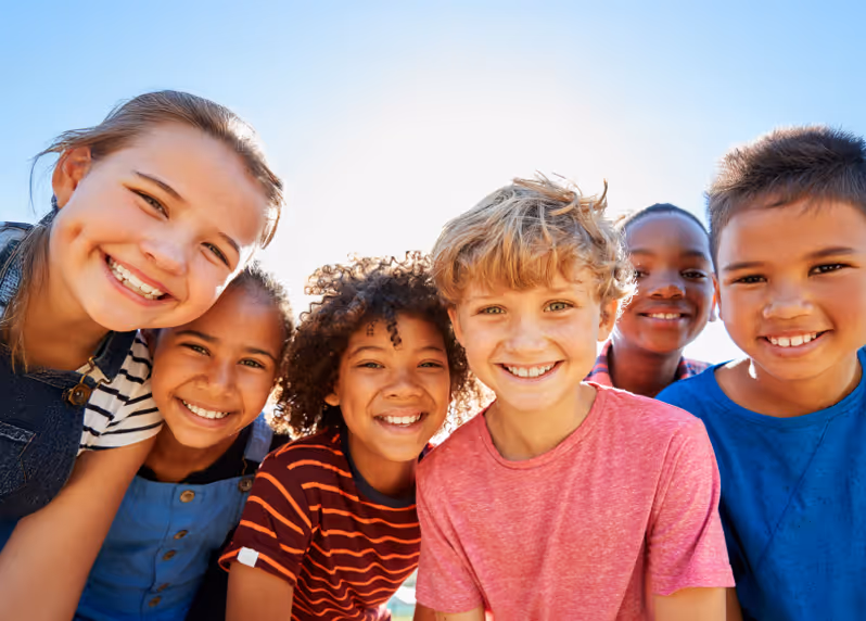 A group of kids huddled together outside smiling into the camera.