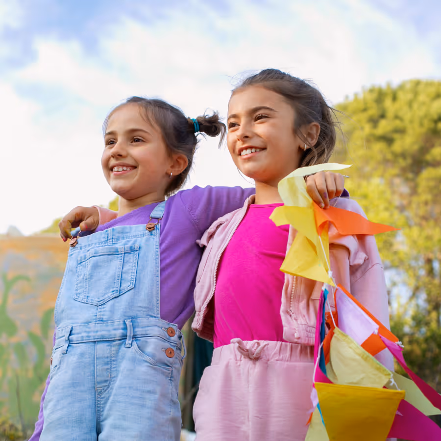 Two little girls smiling off camera outside.