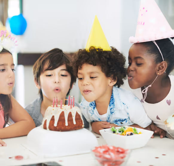 Children at a birthday party blowing out candles on a cake.