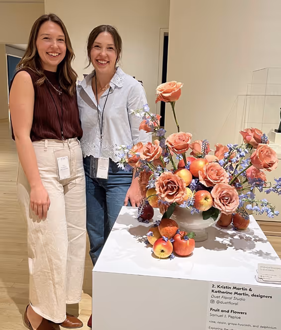 Kristin and Katherine, Founders of Duet Floral Studio, stand in front of floral arrangement at Newfields Art in Bloom