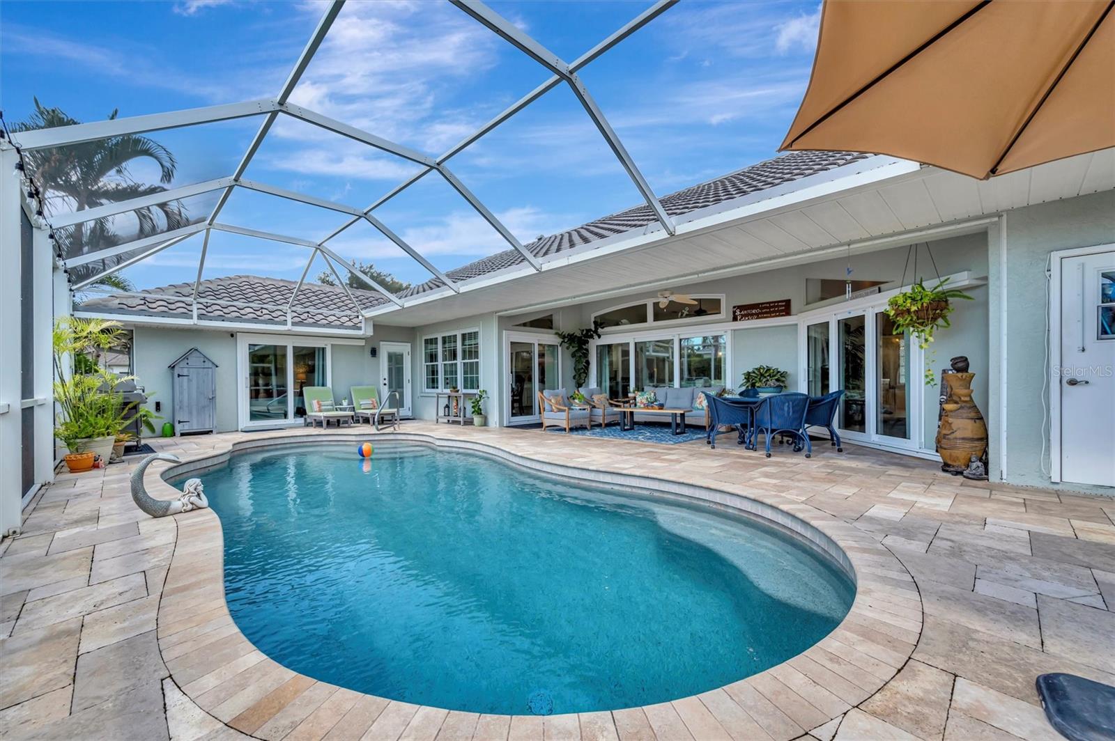 Residential backyard with swimming pool, patio furniture, umbrella, and decorative plants for outdoor leisure and relaxation.