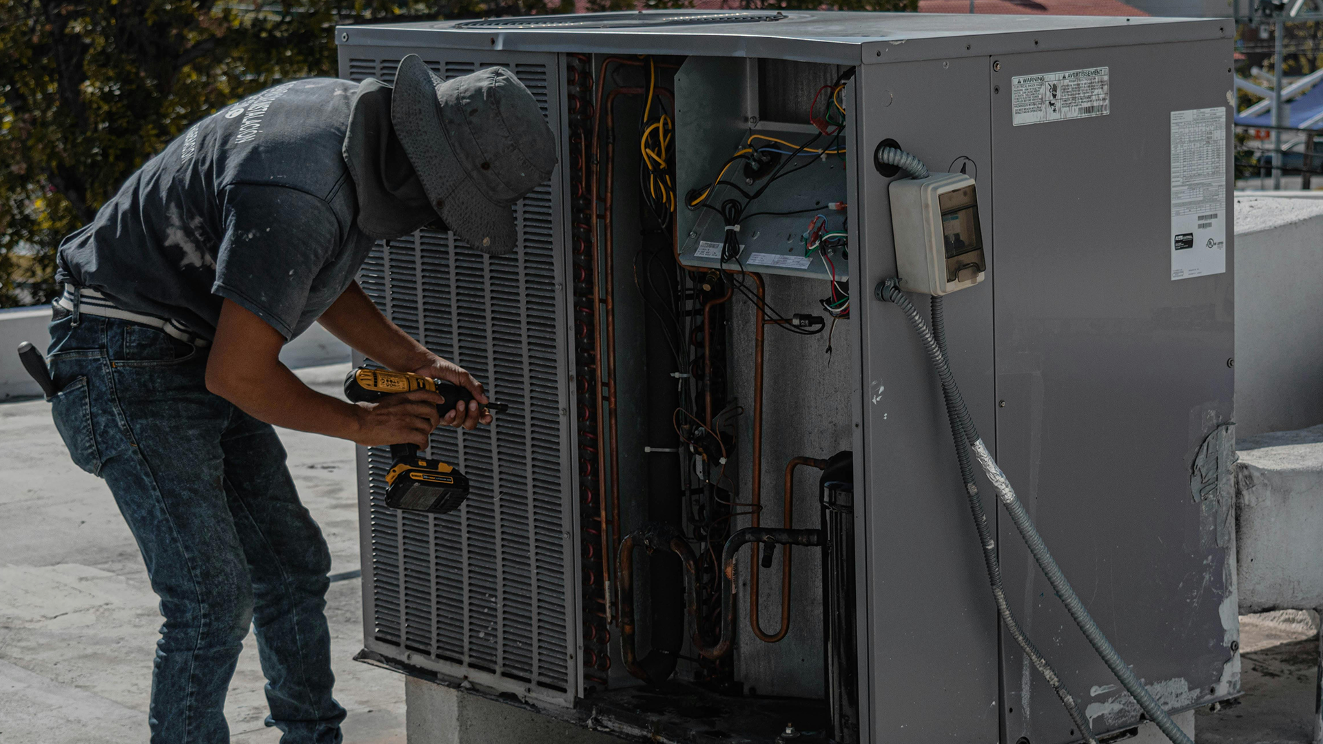 A person fixing an AC unit with power tools outside