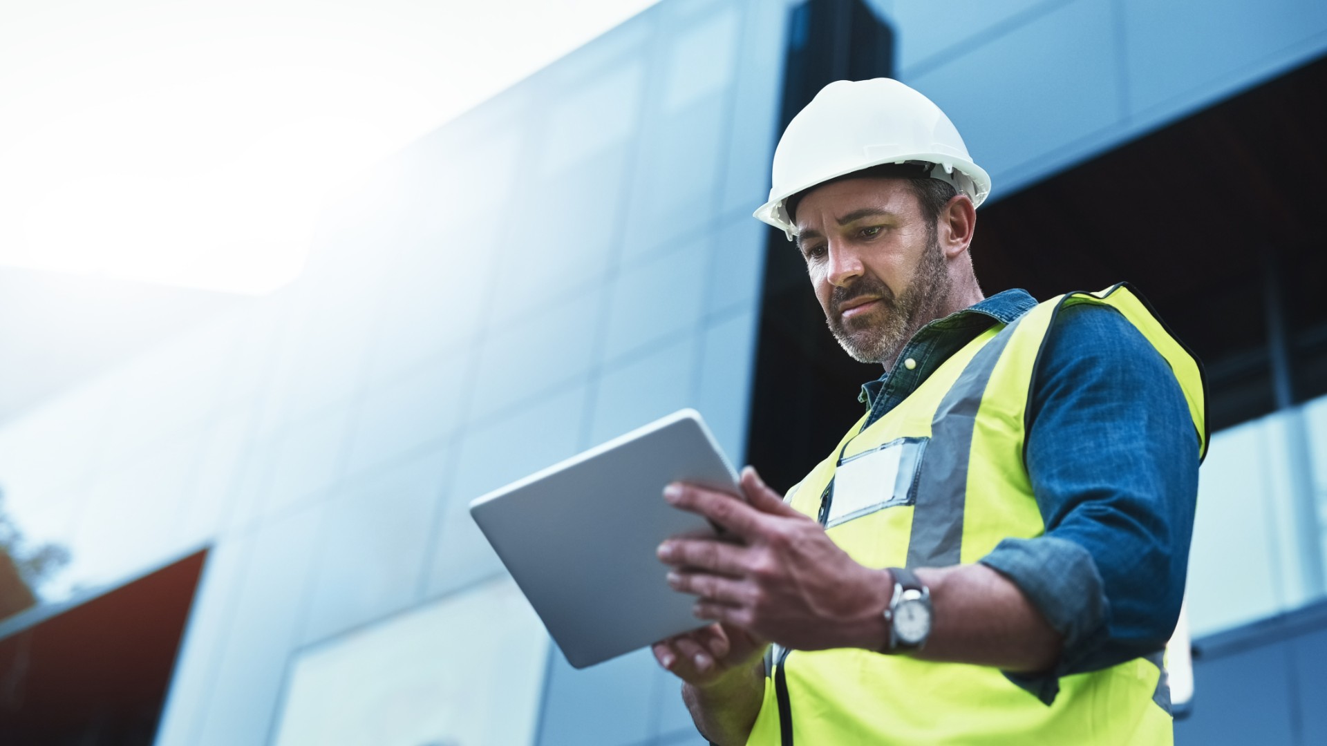 A construction worker looking down at a tablet in his hands