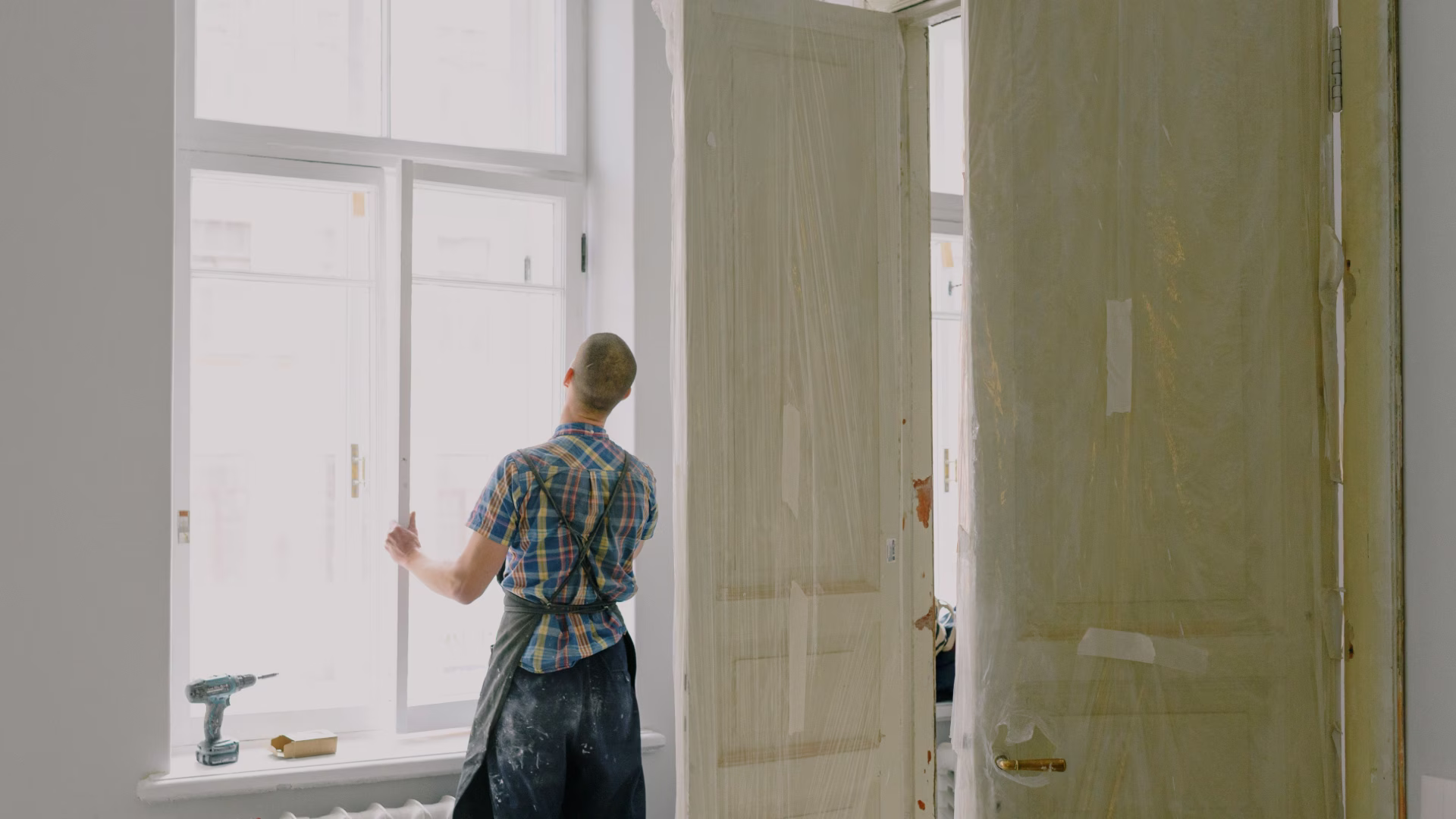 A handyman in an empty room looking to fix a window shutter