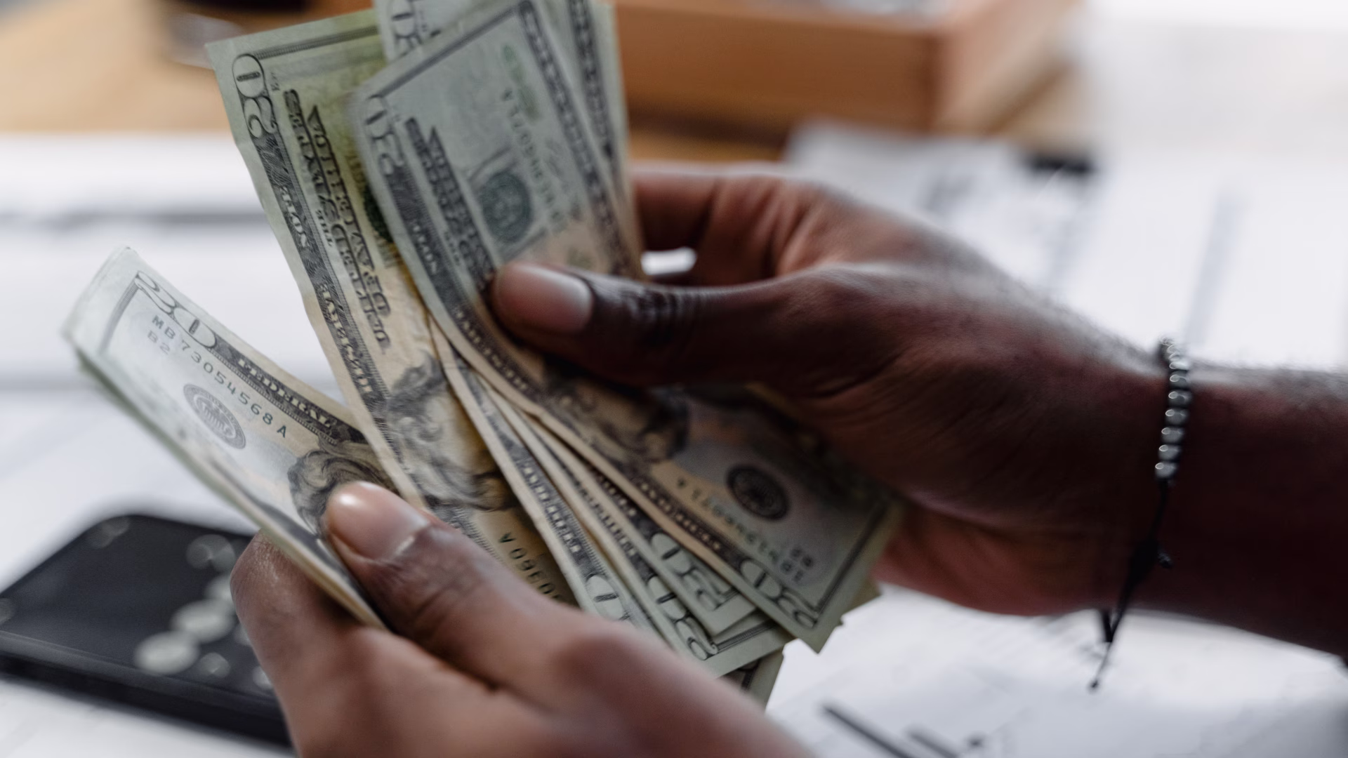 A person counting U.S dollar bills while sitting at a table 