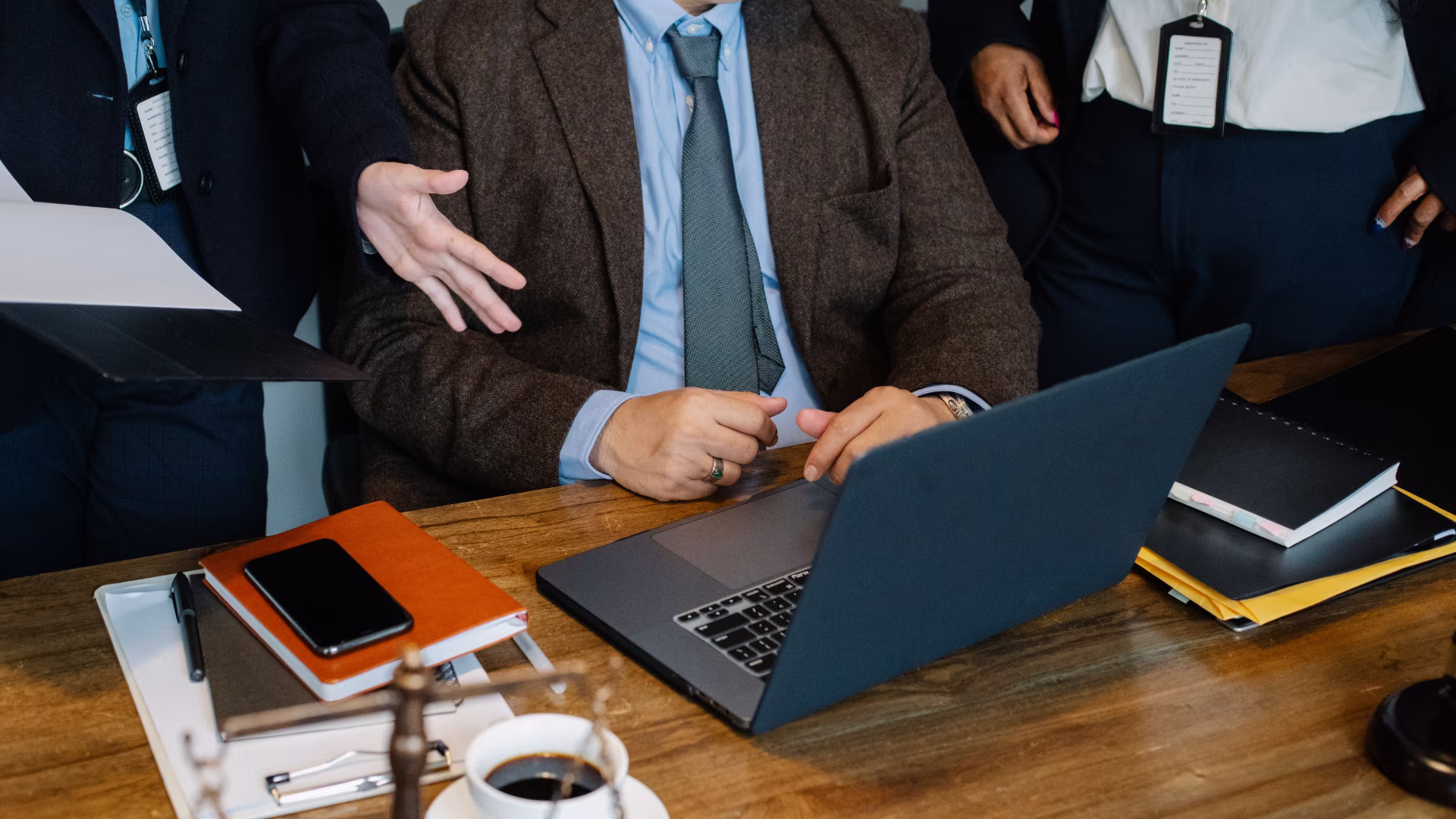 a person sitting at a desk with their laptop open along with two other people standing alongside them