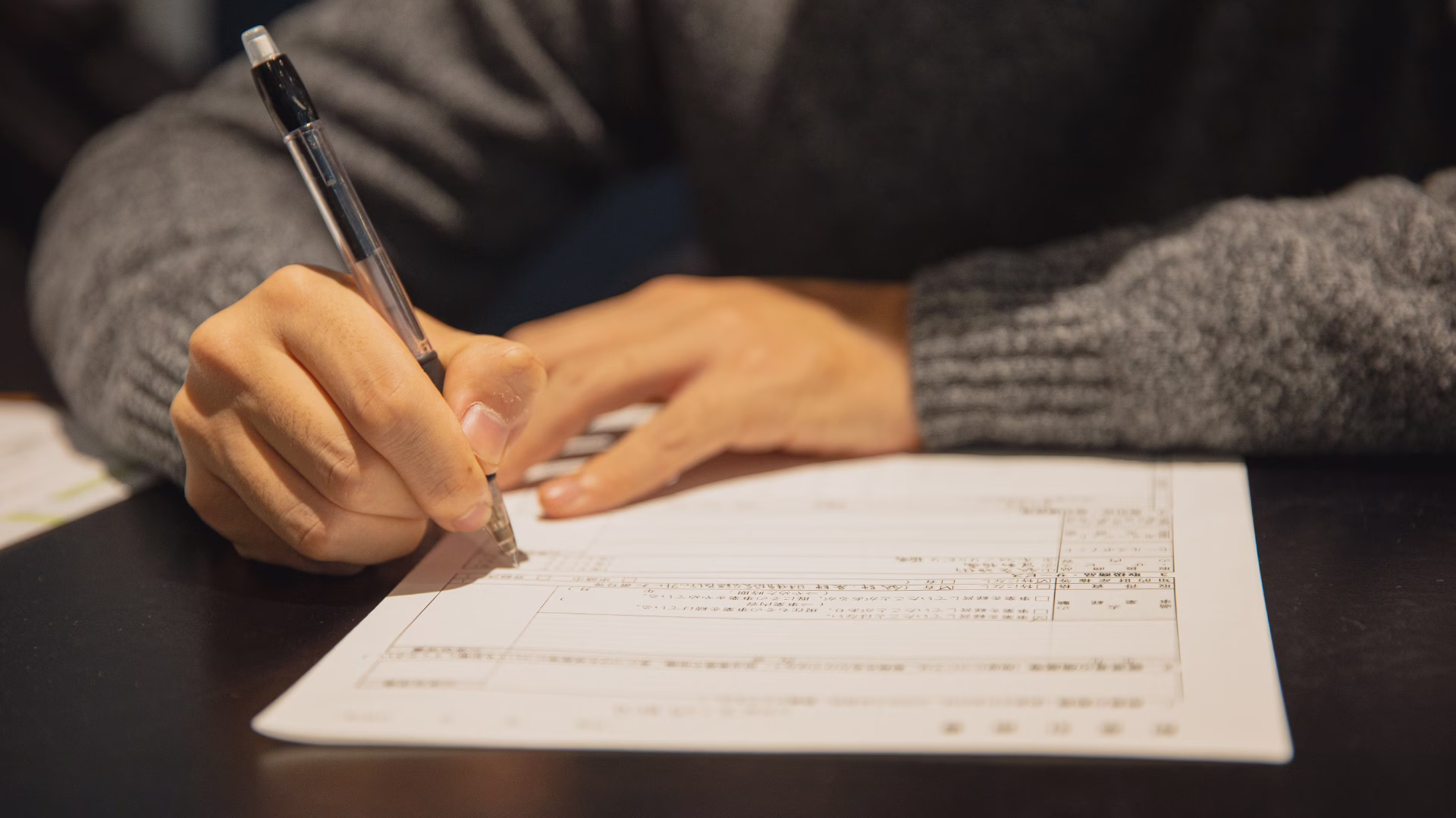 A person sitting at a table writing something on a piece of paper
