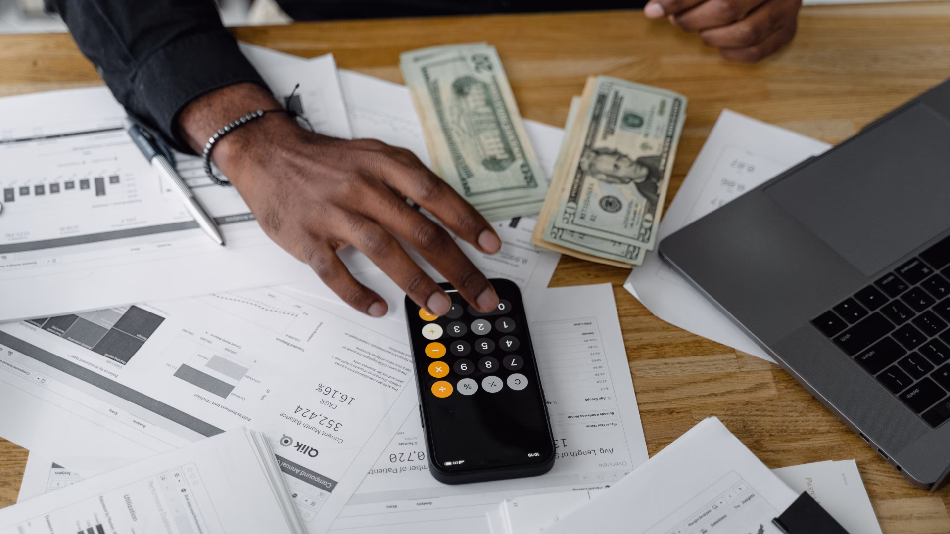 A person sitting a desk looking at their invoicing management software, along with documents and cash