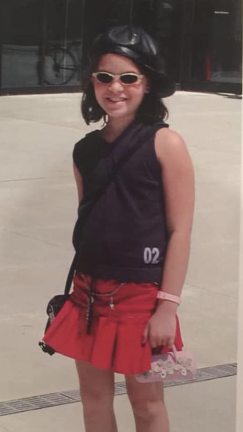 Picture of Gabi at around 10 years old, wearing a leather hat, pink mini skirt, and tank top.
