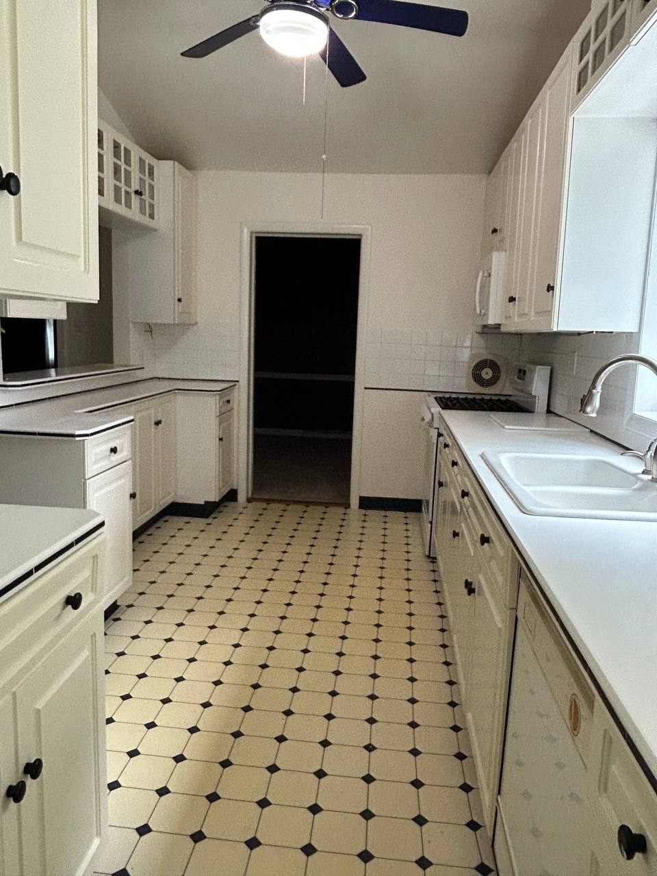 Galley kitchen with white cabinets, ceiling fan and dotted tile floor