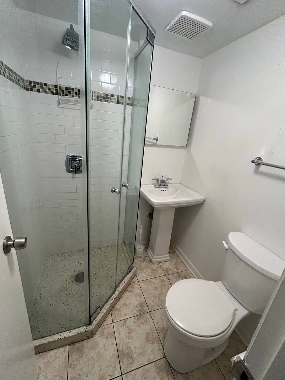 Small bathroom with glass corner shower, pedestal sink and toilet