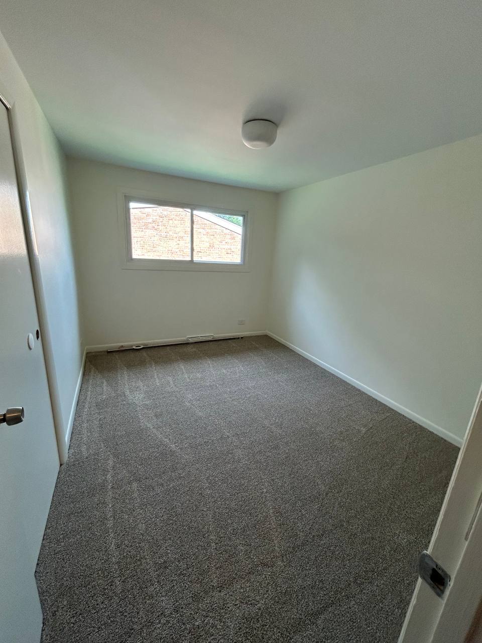 Empty bedroom with fresh gray carpet, white walls and one window