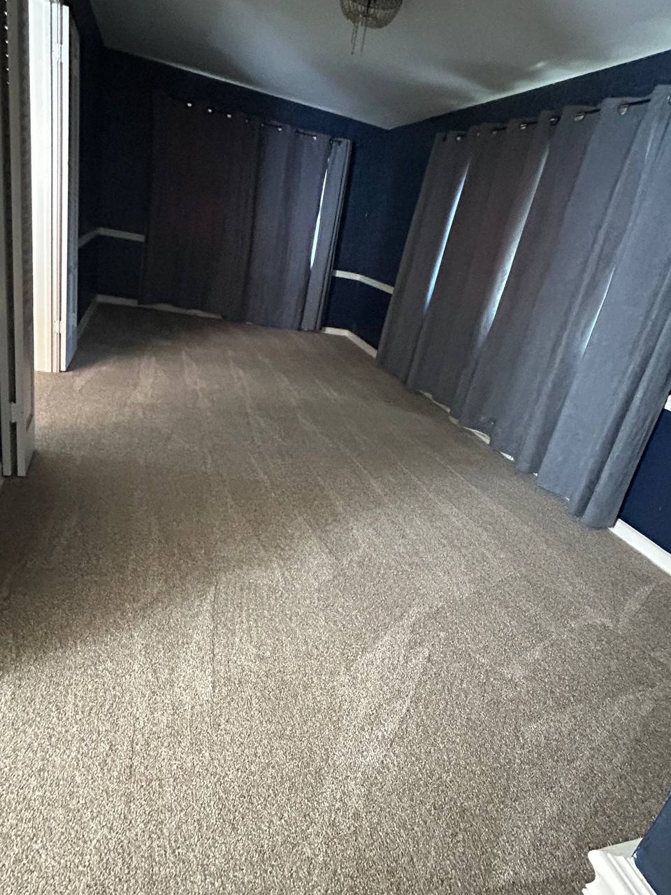Empty bedroom with dark blue walls, gray curtains and beige carpet