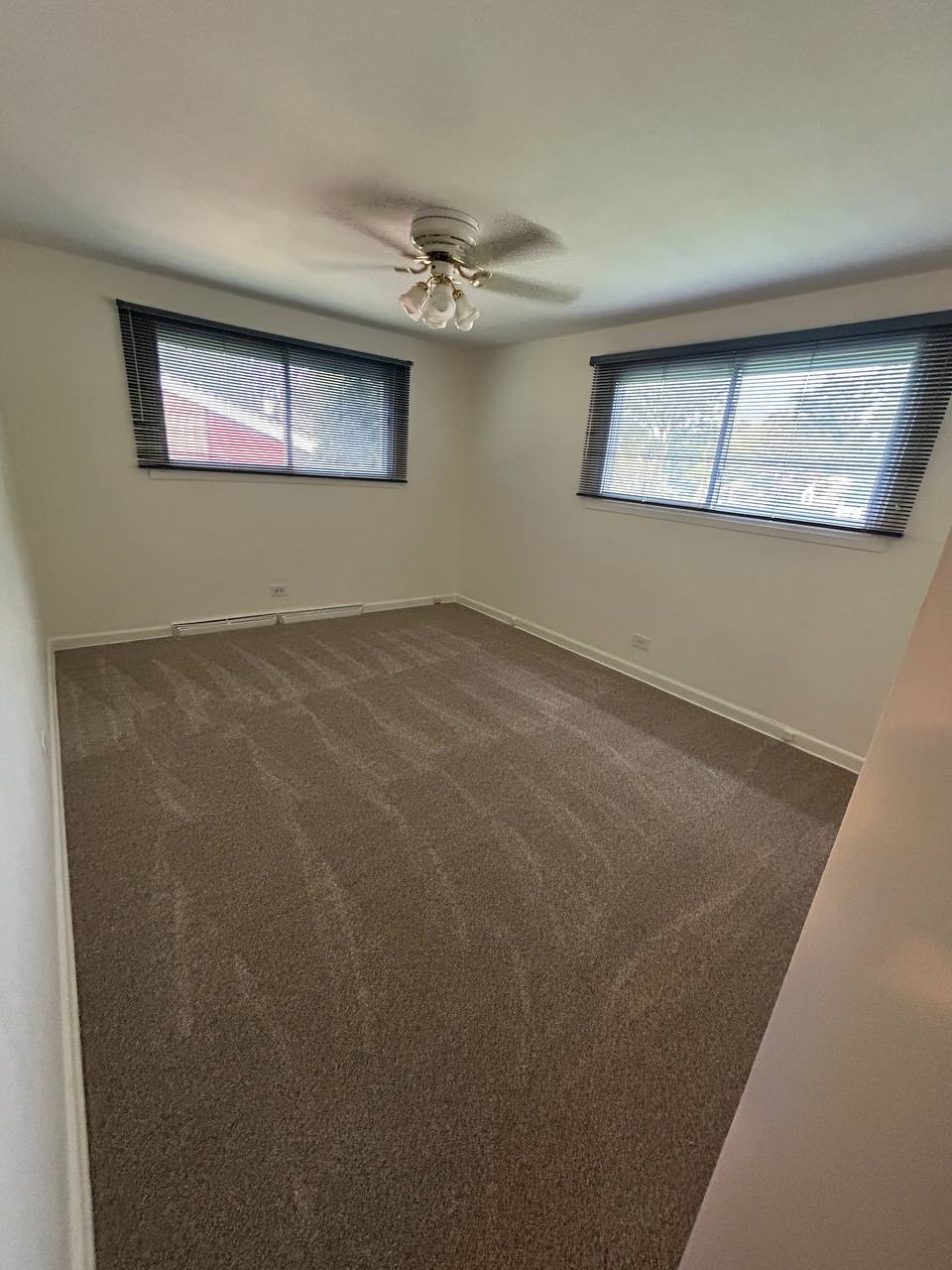 Empty bedroom with brown carpet, two windows and ceiling fan