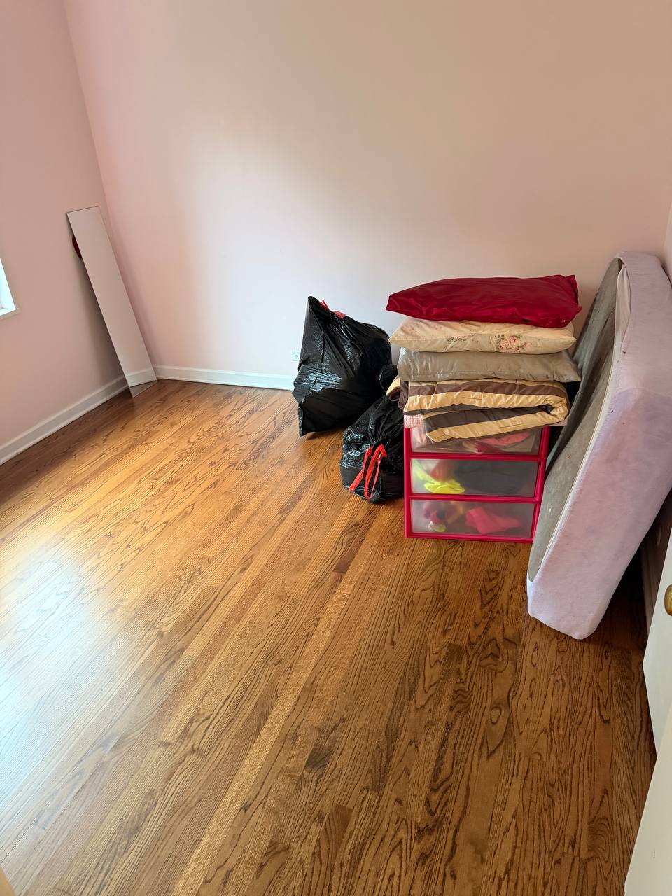Pink bedroom with oak floor, folded bedding and plastic storage drawers