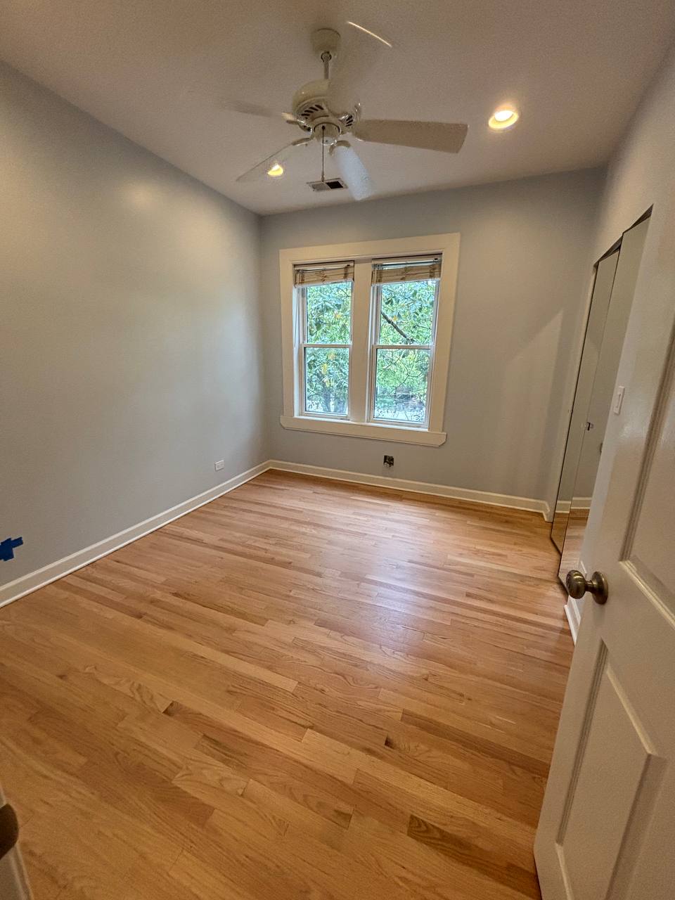 Empty bedroom with light oak floor, ceiling fan and double window