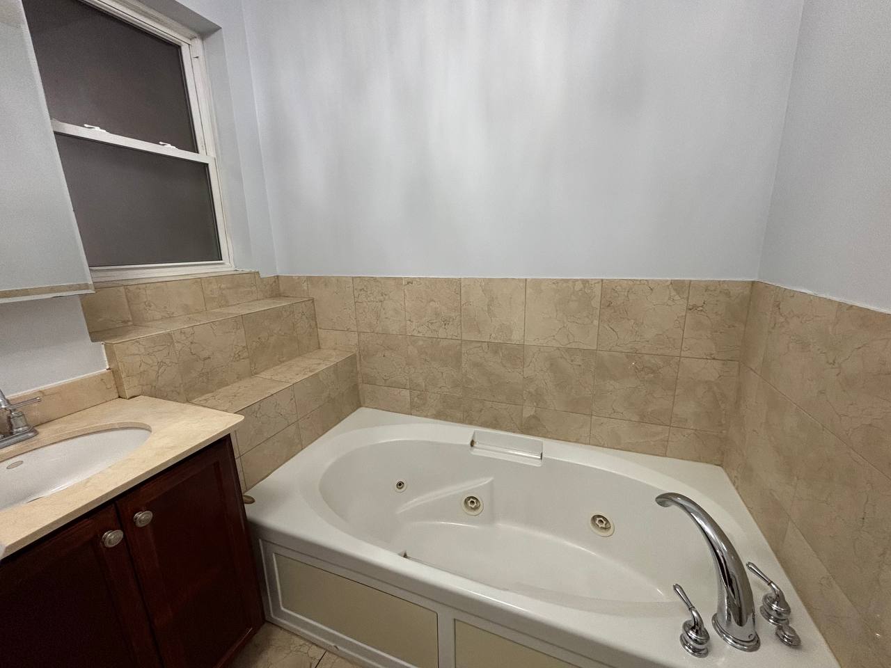Beige tile bathroom with corner jetted tub and wood vanity