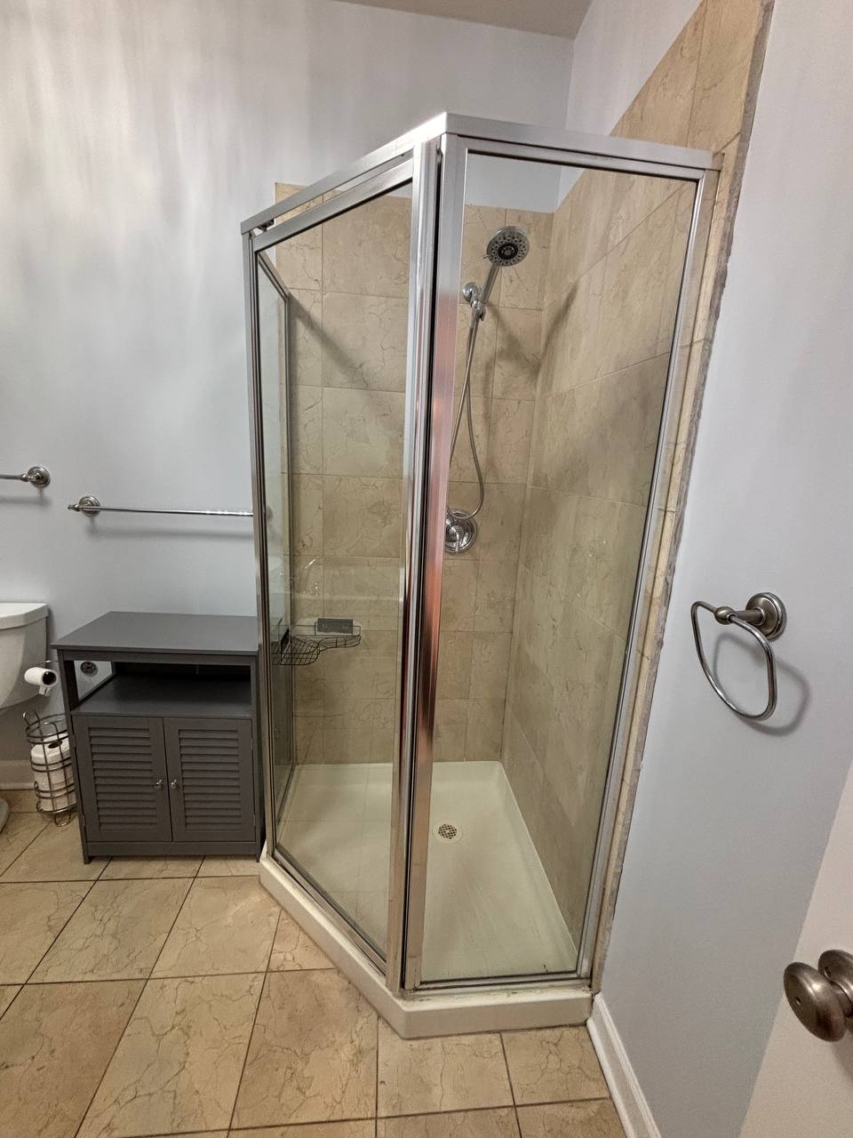 Corner glass shower stall with beige tile and gray cabinet