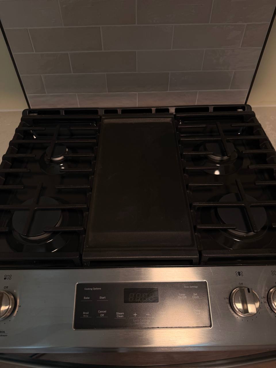Cleaned black gas cooktop with center griddle and gray subway tile