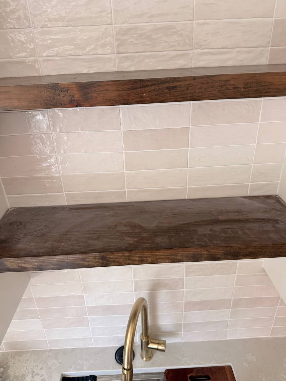 Wood floating shelves on white subway tile above a gold faucet