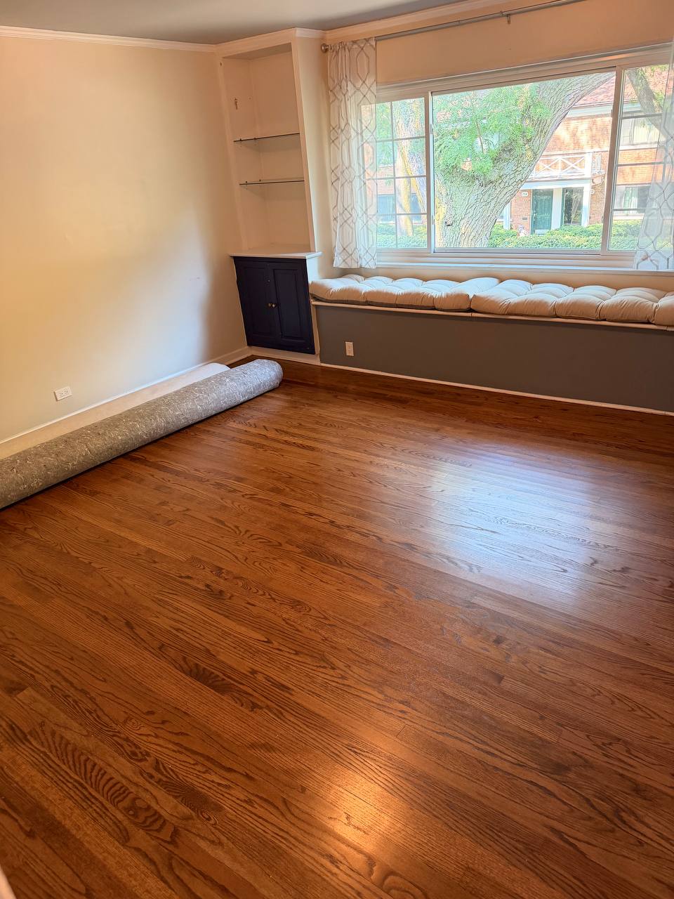 Living room with polished hardwood floor, window seat and rolled rug