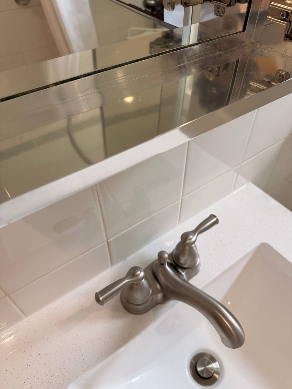 Brushed nickel bathroom faucet with white sink, tile and mirror shelf