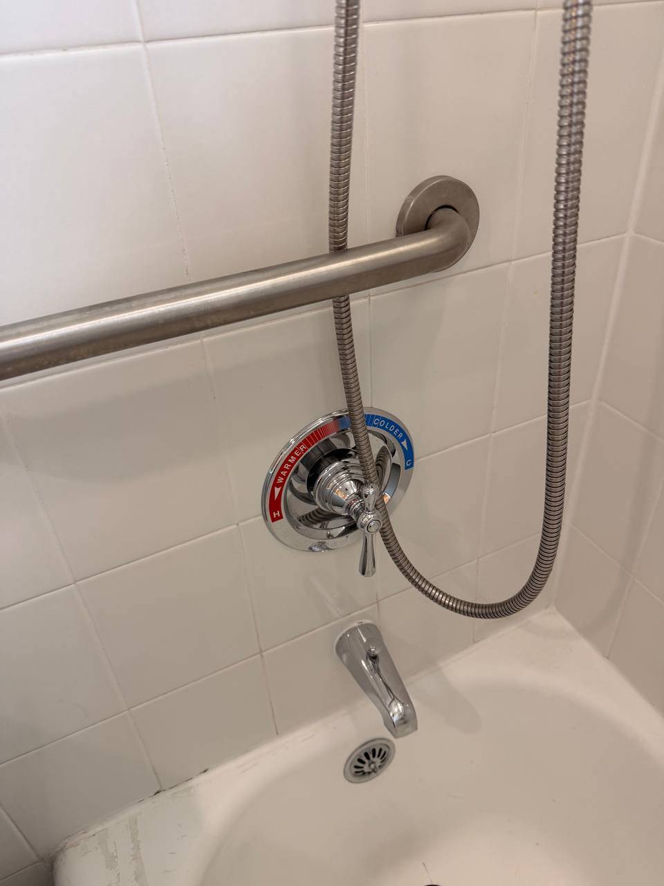 White tile shower wall with chrome faucet, grab bar and hose