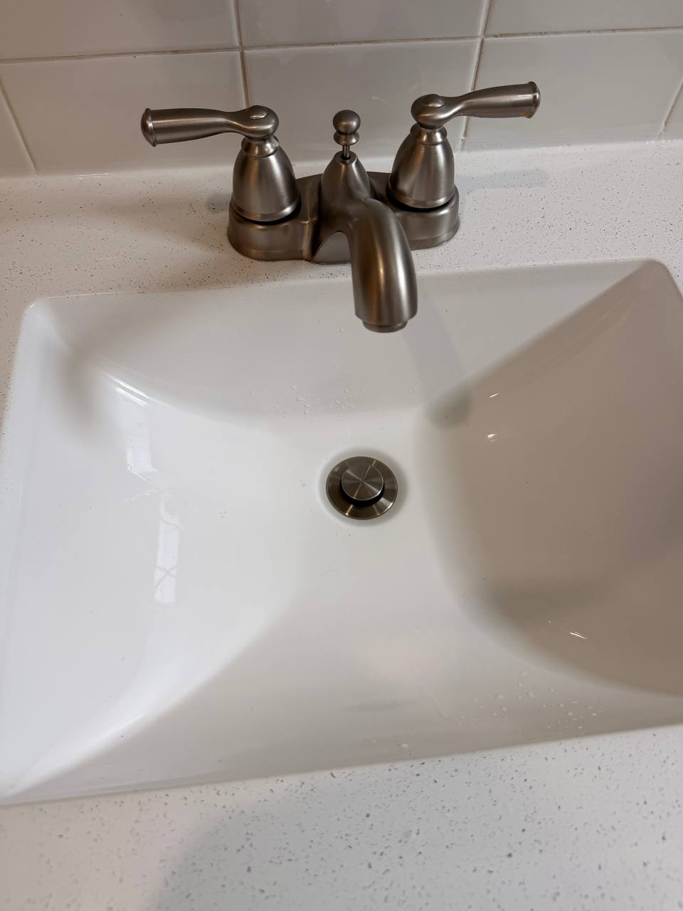 White bathroom sink with brushed nickel faucet on speckled counter