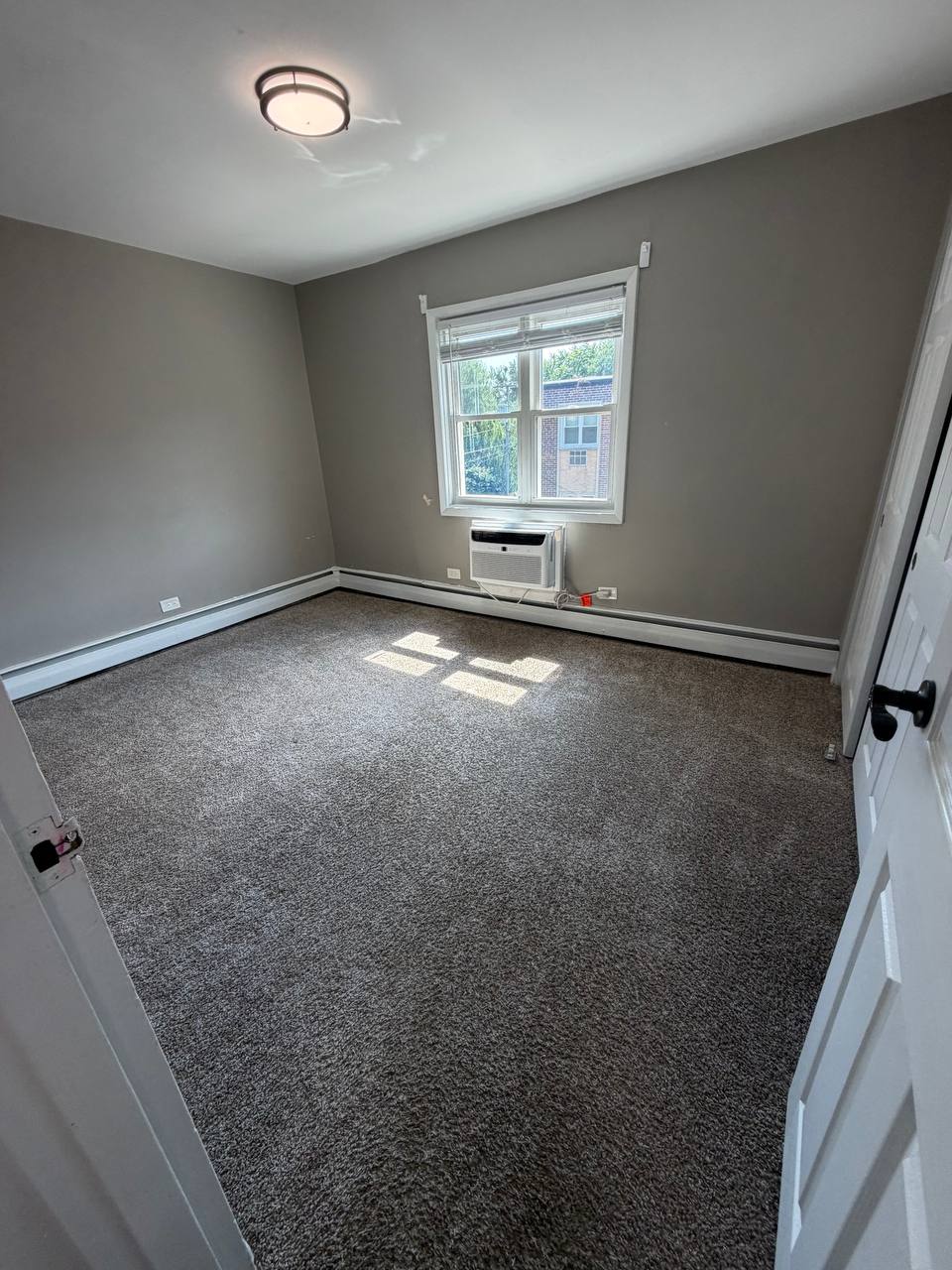 Empty gray bedroom with carpet, window unit and sunlight