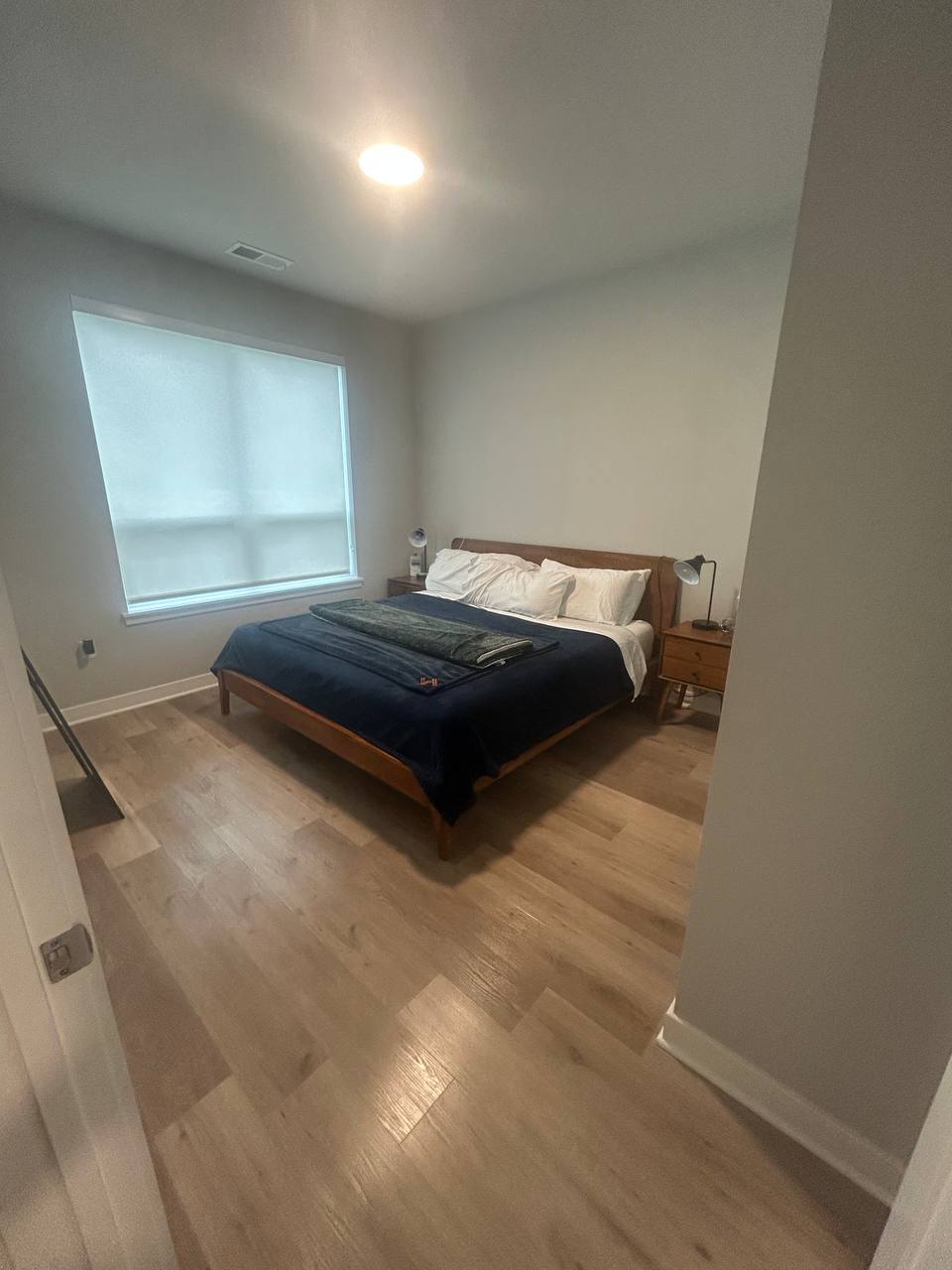 Bedroom with wood bed frame, navy blanket and light wood floor