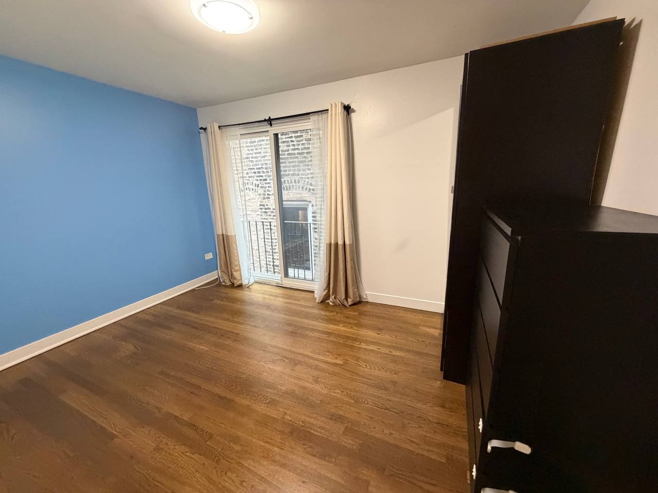 Room with blue accent wall, wood floor, curtains and black dresser