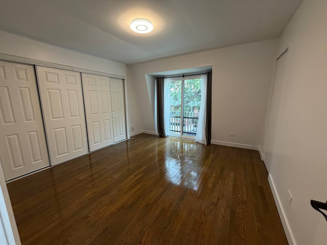 Empty bedroom with dark hardwood floor, closet doors and balcony door