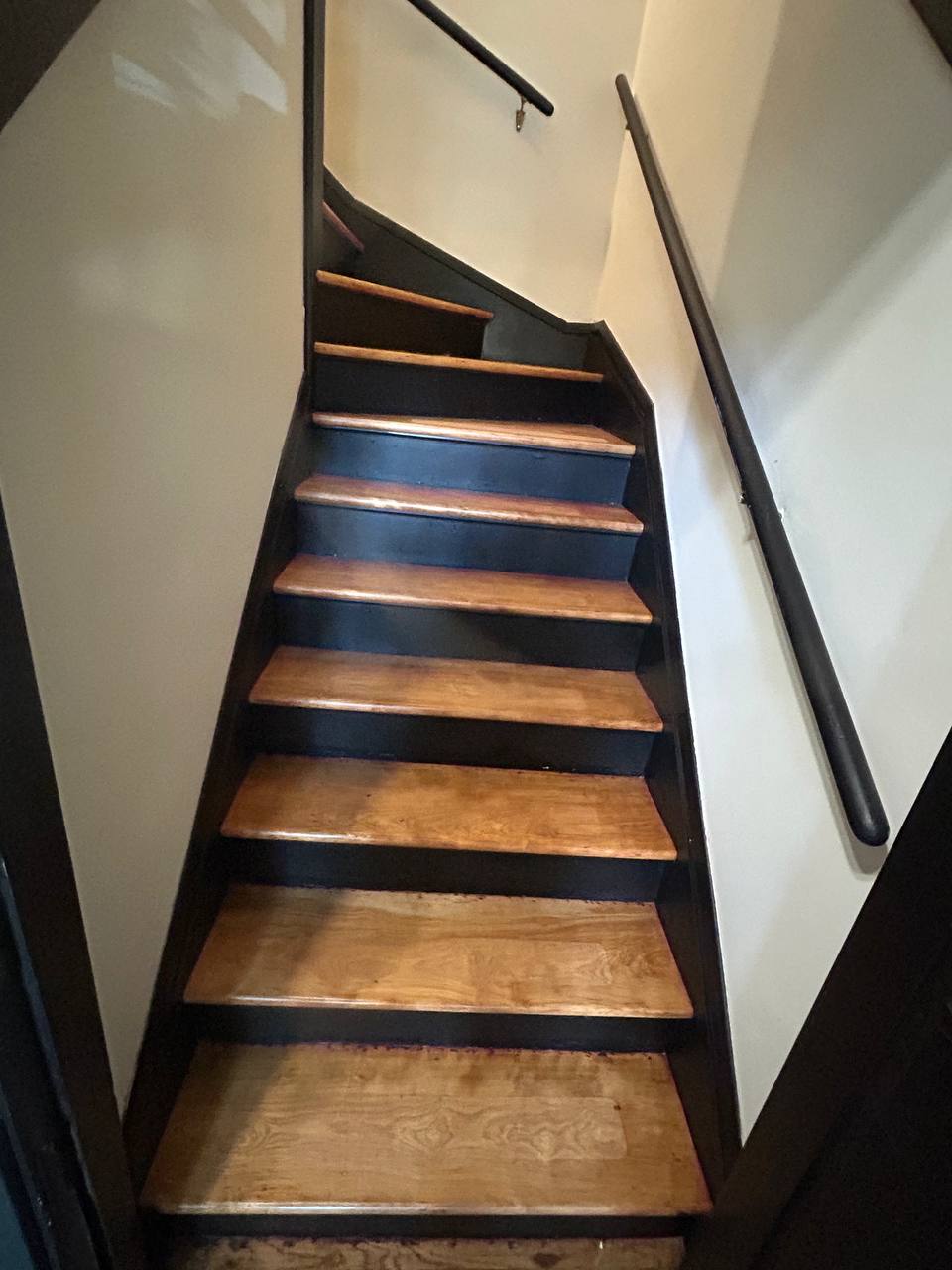 Narrow wooden staircase with dark risers and black handrail