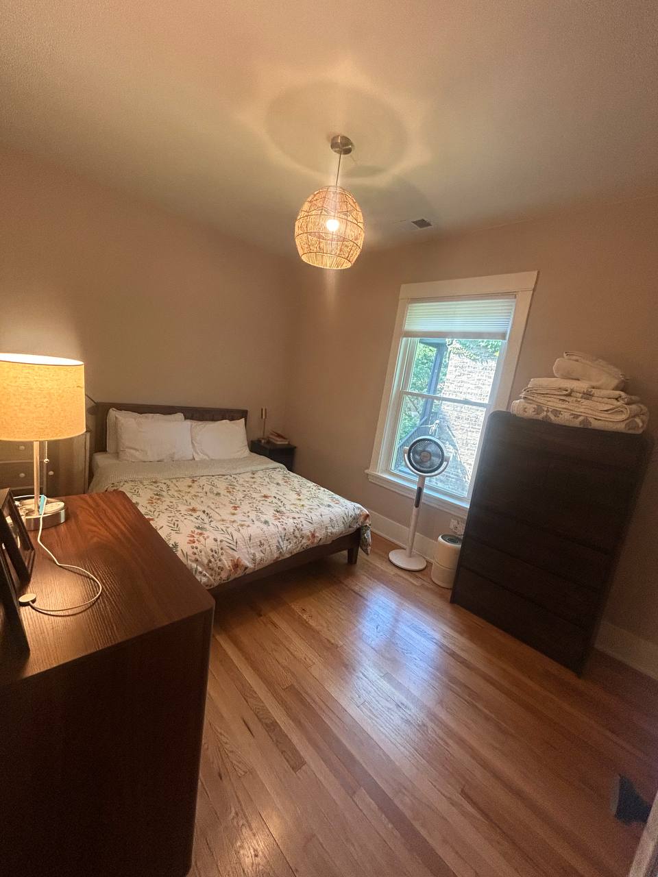 Small bedroom with floral bedding, lamp, fan and wood floor