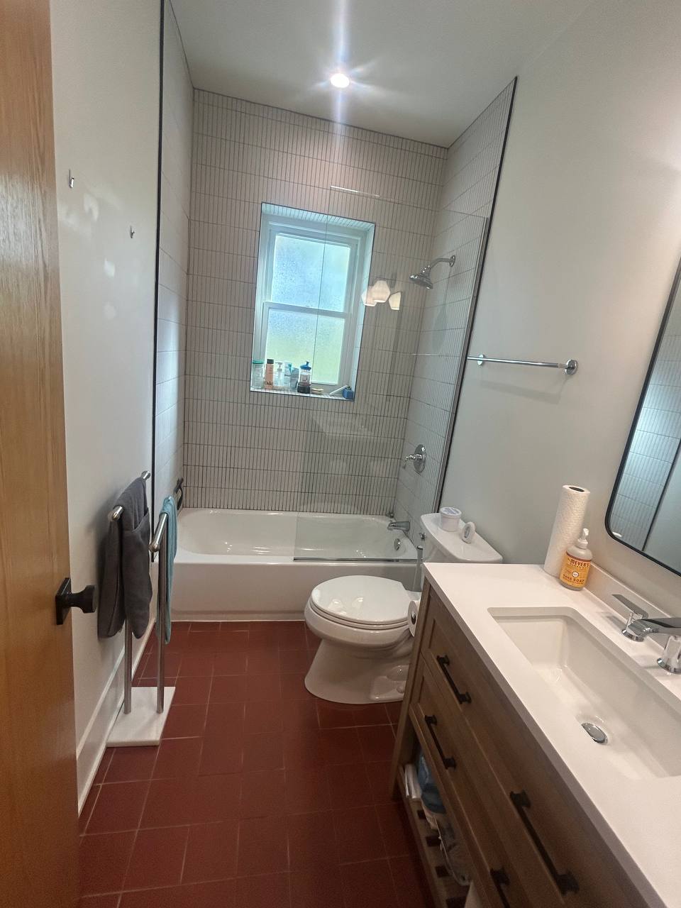 Bathroom with white tiled tub, red floor tile and wood vanity