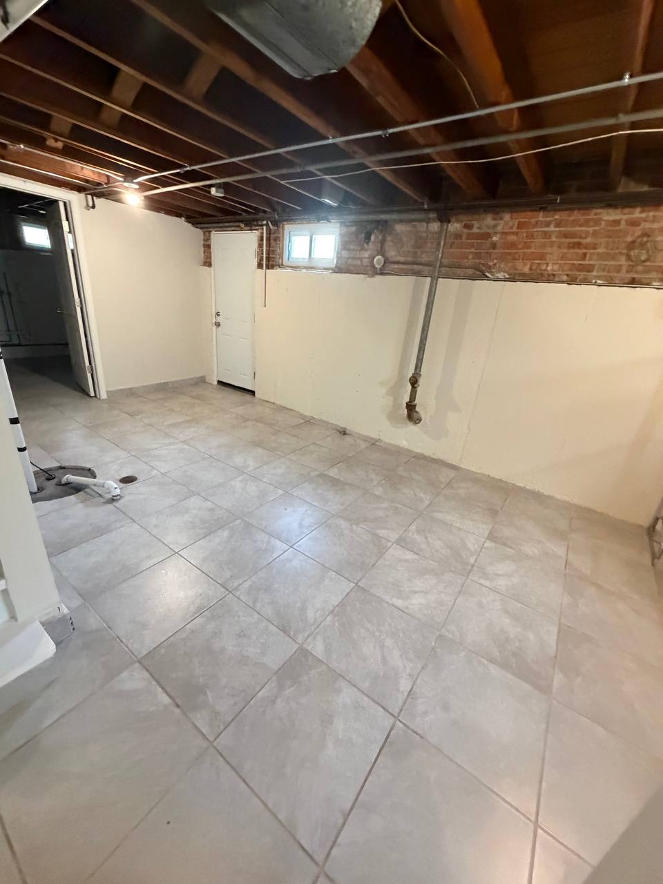 Basement with gray tile floor, exposed joists and brick wall