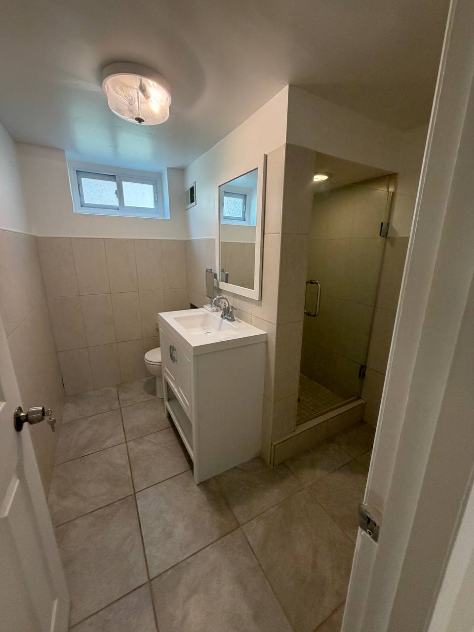 Basement bathroom with beige tile, glass shower, white vanity and toilet