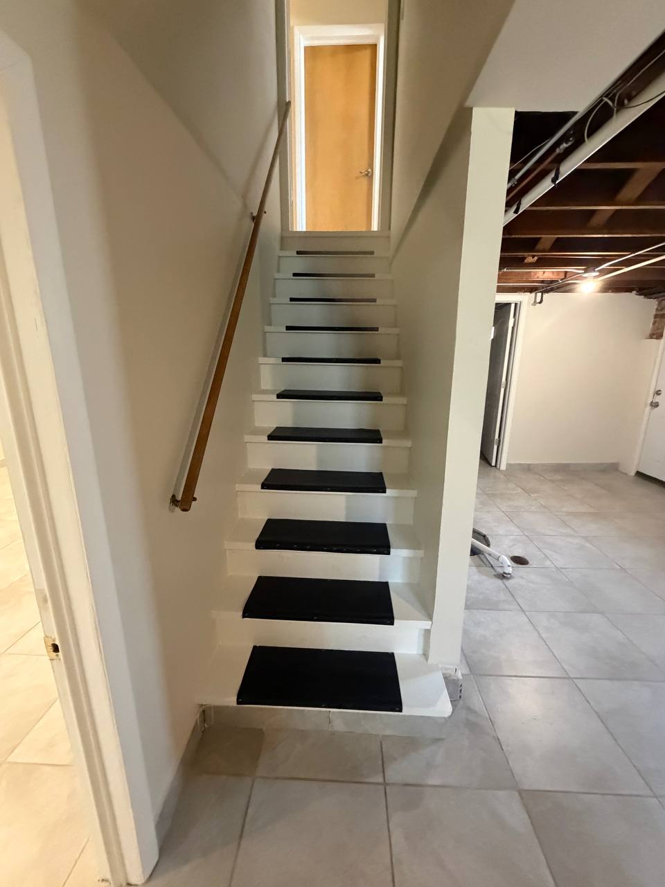 White basement staircase with black treads and tile floor below