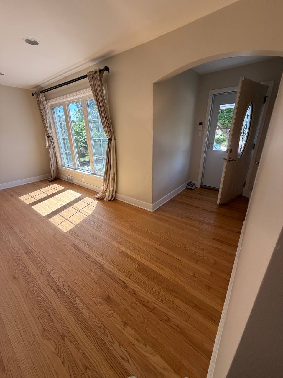 Empty living room with hardwood floor, tall window and front door