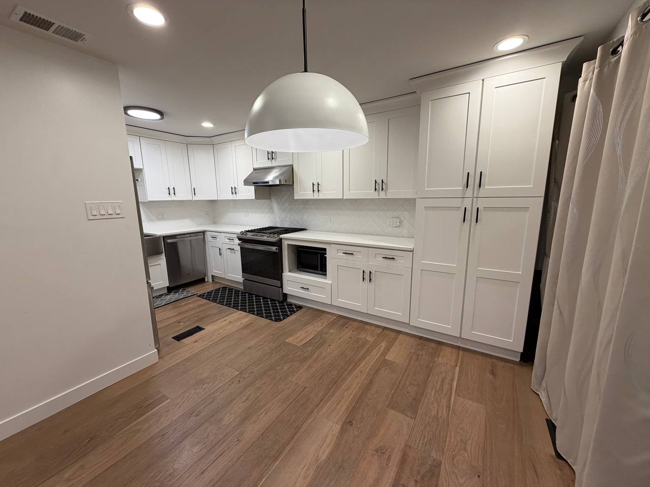 White kitchen with large dome pendant light and herringbone backsplash