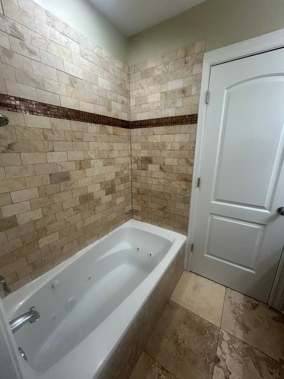 Whirlpool tub with beige stone tile surround beside a white door