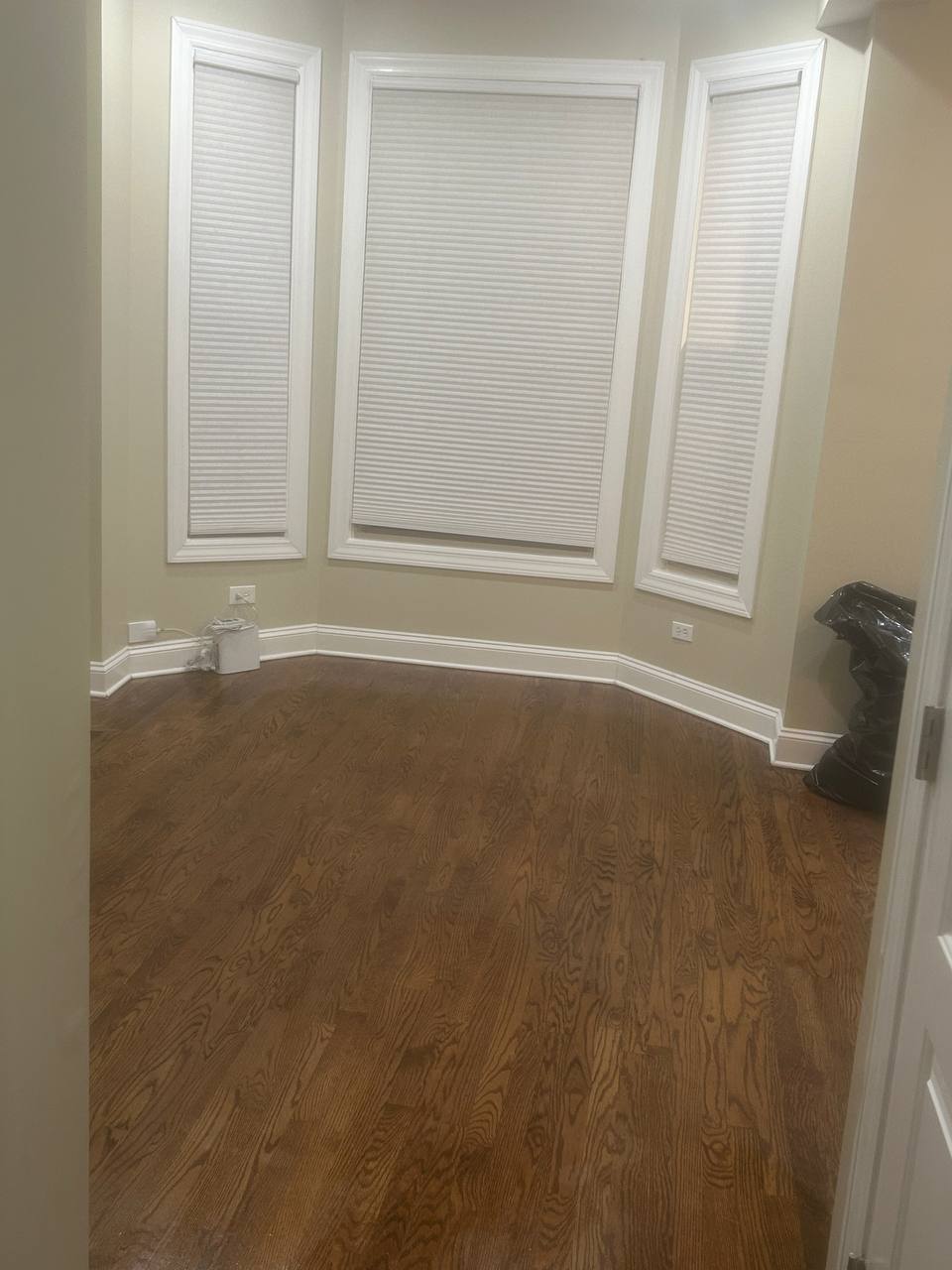 Empty room with hardwood floor and three windows with white shades