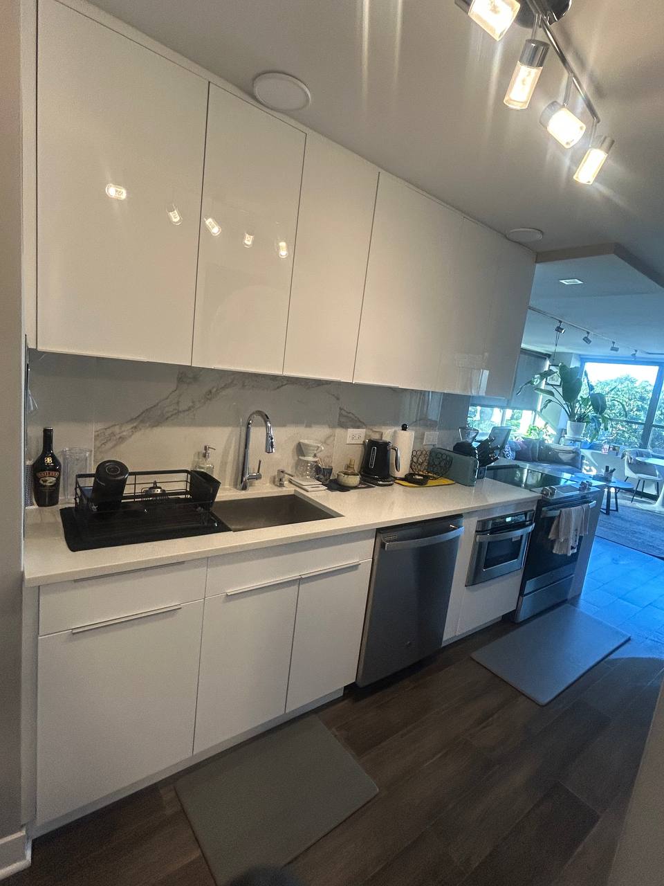Glossy white kitchen with marble backsplash, dish rack and track lighting