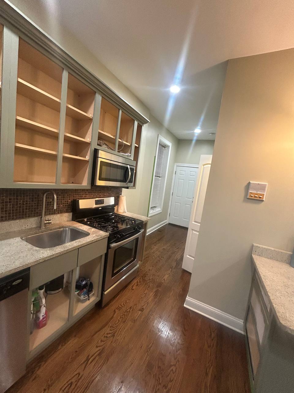 Galley kitchen with open gray cabinets, stainless range and dark wood floor