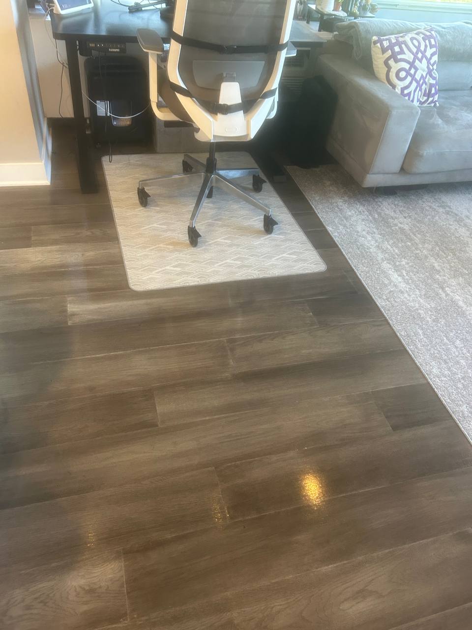 Wood floor beside a desk chair mat, standing desk and gray sofa