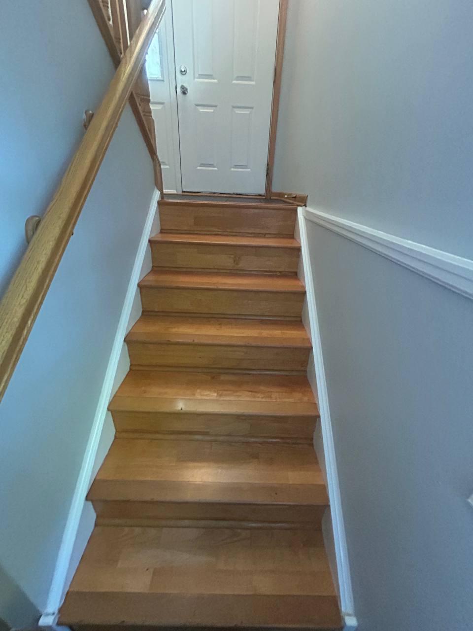 Wood staircase with handrail leading up to a white front door