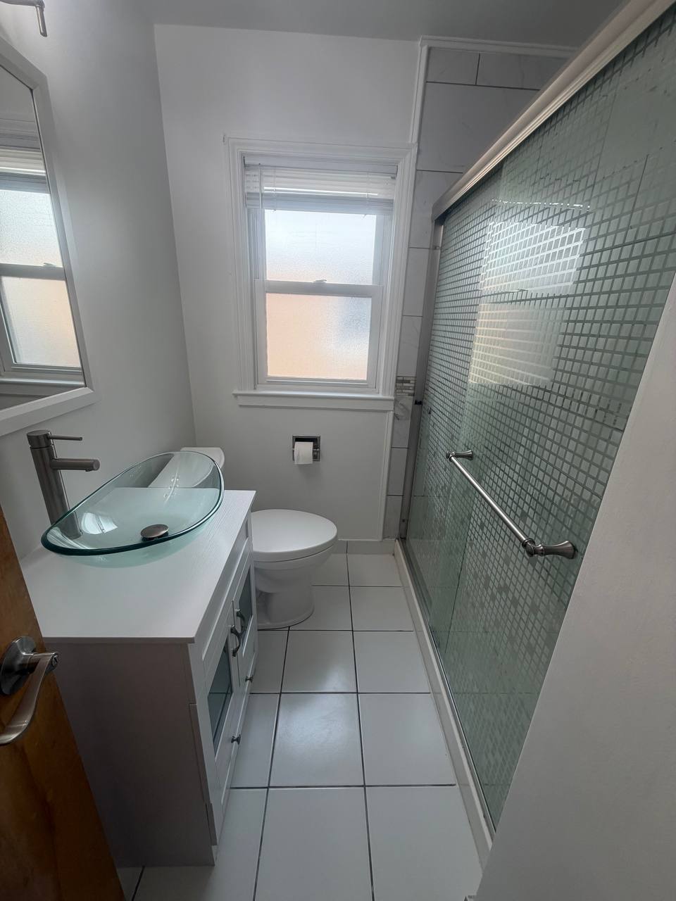 Narrow bathroom with glass vessel sink, toilet and mosaic tile shower door