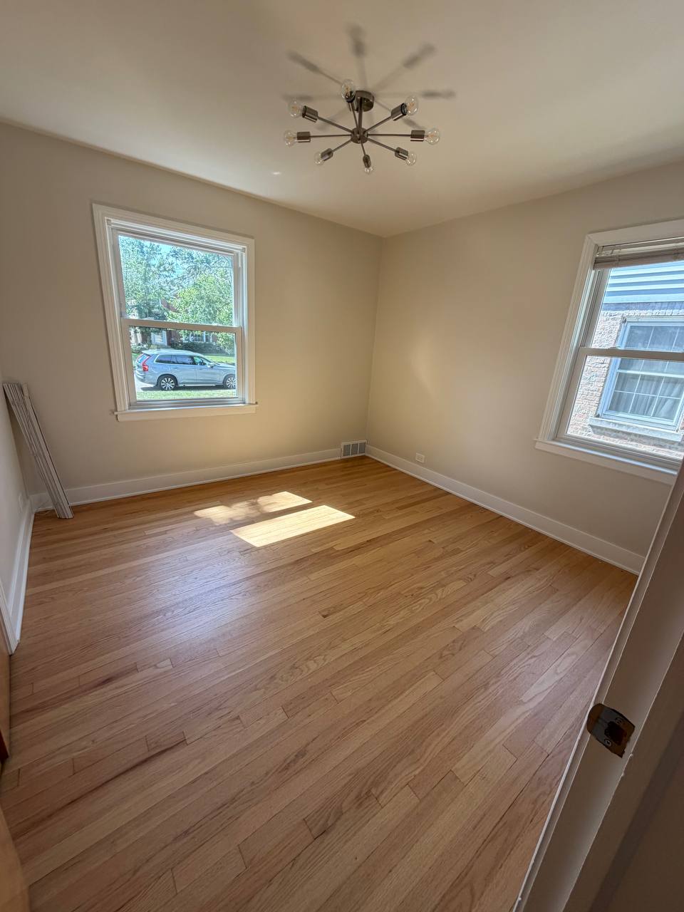 Empty bedroom with wood floor, two windows and sputnik light fixture