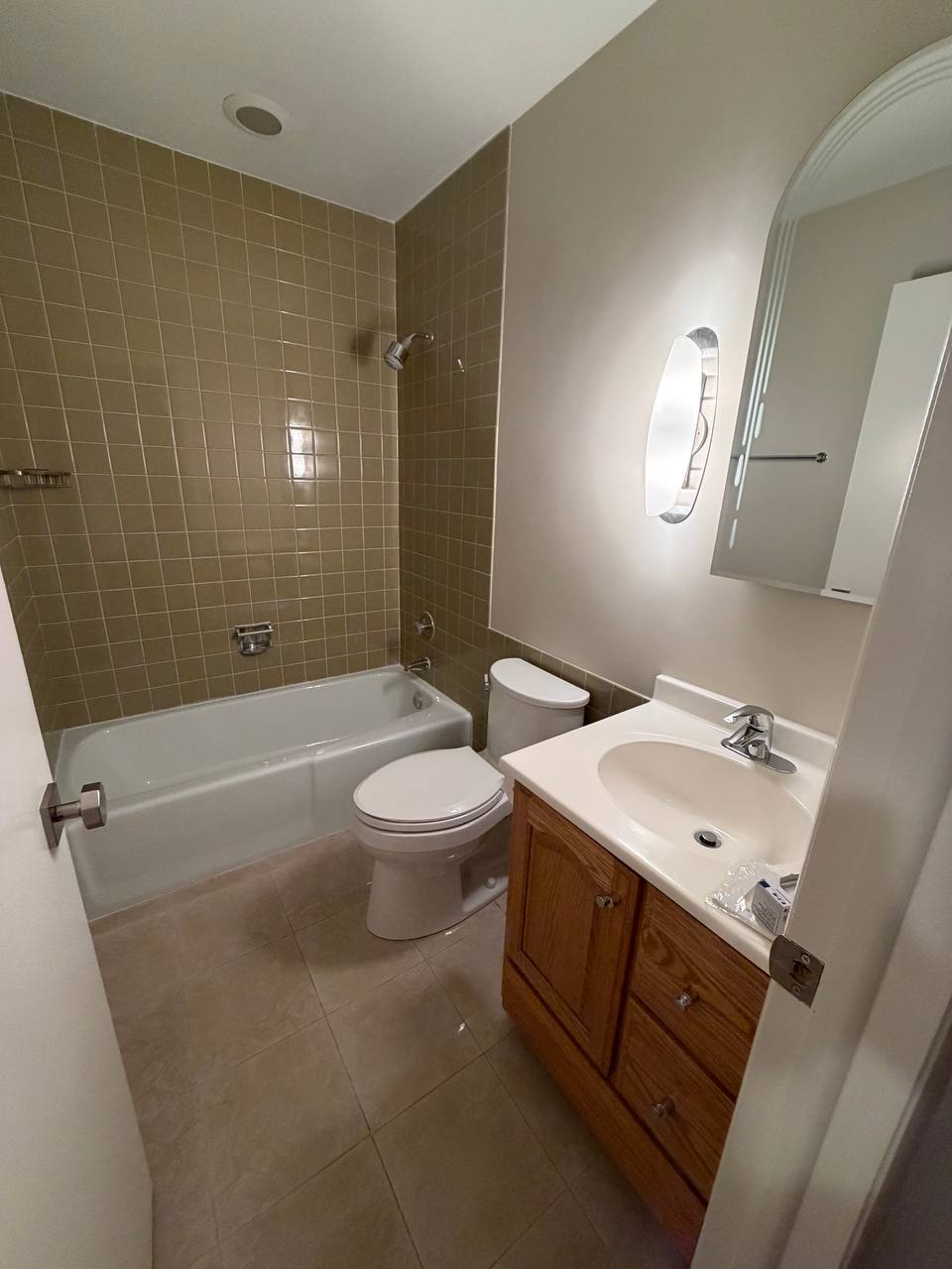 Bathroom with olive tile tub surround, toilet and oak vanity