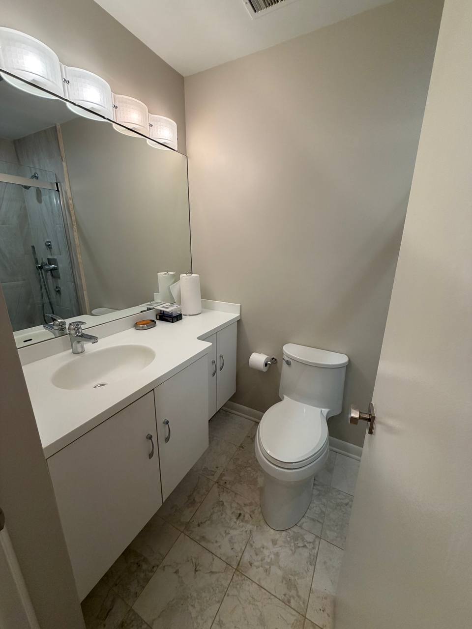 Beige bathroom with white vanity, wide mirror and toilet